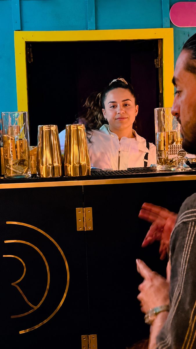Bartender preparando cócteles de noche detrás de la barra negra con logo dorado